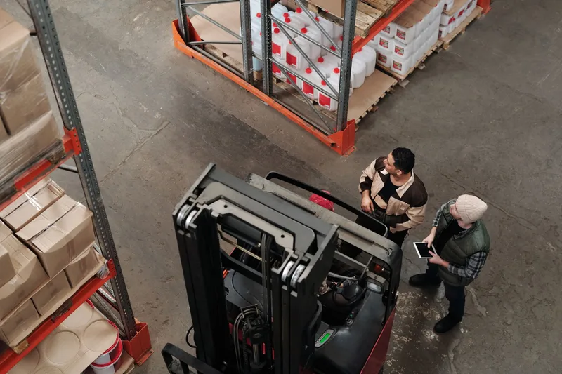Dua anggota crew warehouse berkoordinasi dekat forklift saat pergantian shift