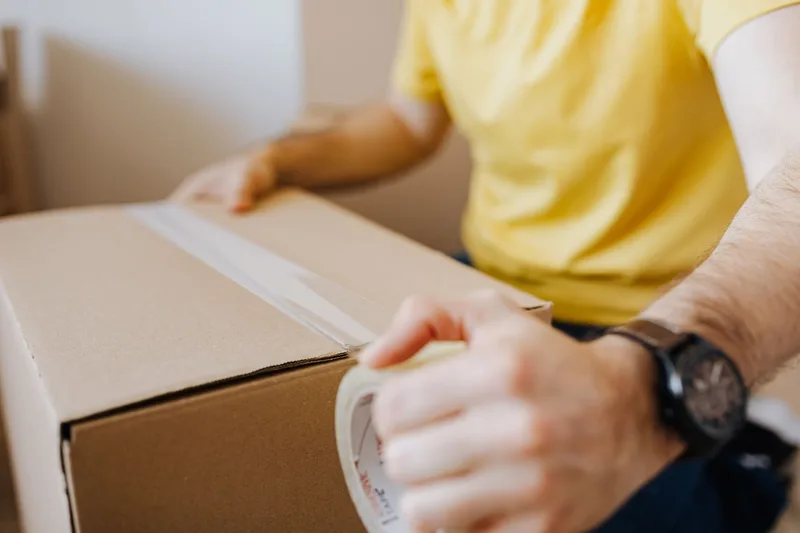 Close-up of hands taping a cardboard box shut with a roll of packing tape