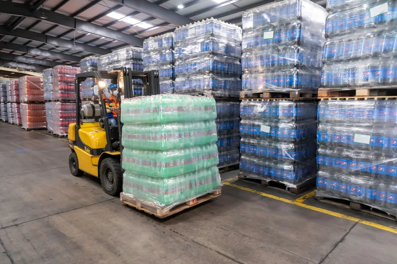 Forklift operator moving stacked pallets in a busy warehouse, representing a fulfilled procurement order arriving at the warehouse
