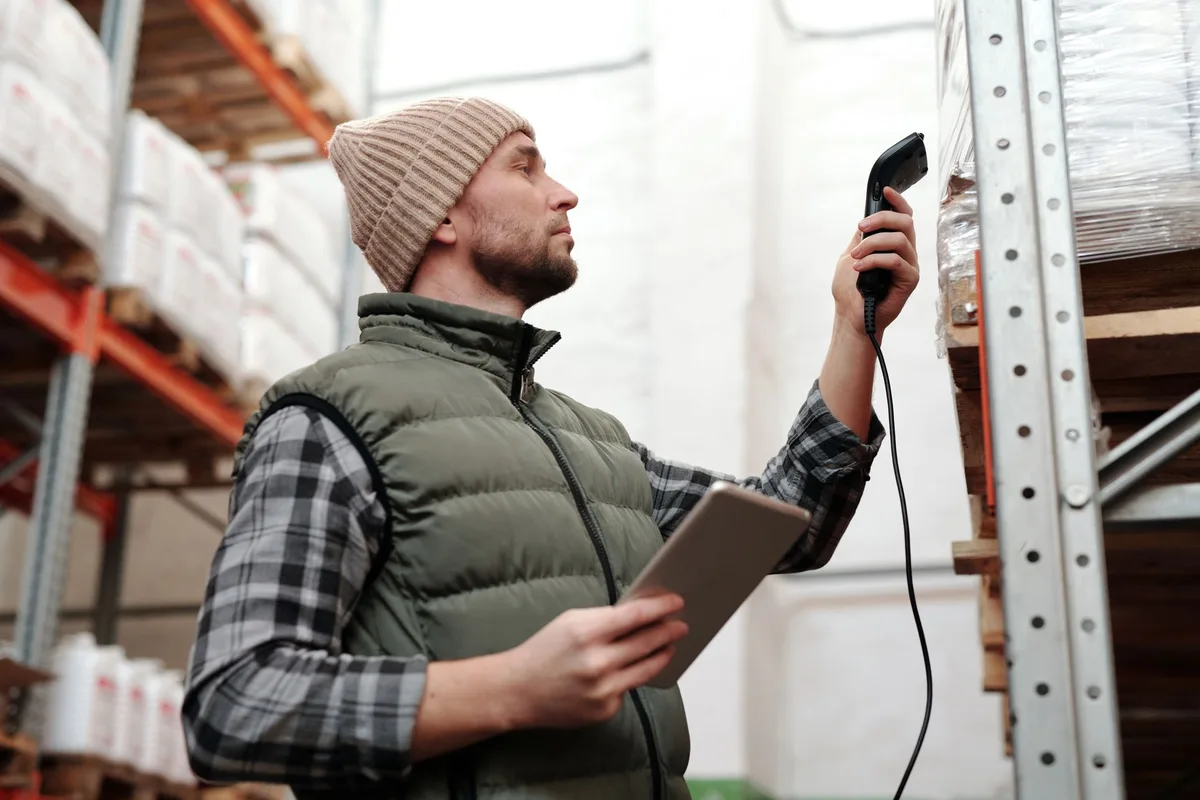 Staf gudang menggunakan scanner barcode dan tablet untuk mengelola inventory dengan warehouse system management software