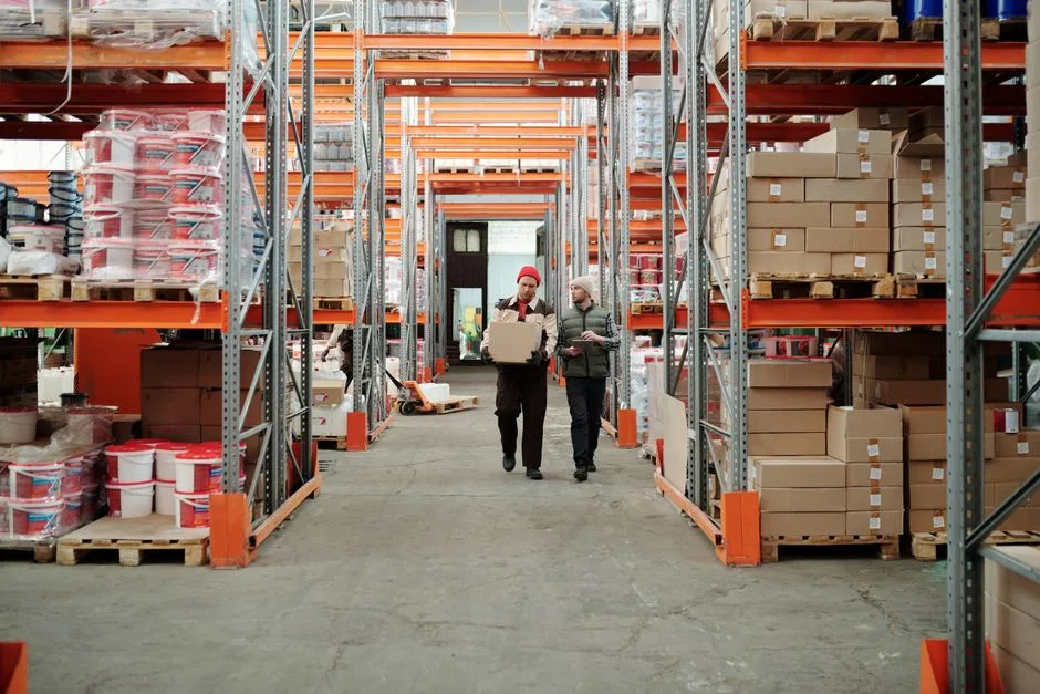 Two workers handling packages inside a warehouse with shelves stocked with boxes, representing systematic warehouse management workflow